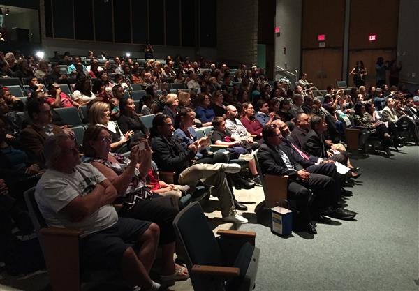 About 150 people seated inside a stadium style theatre